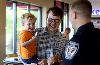 Plymouth police officer talking with a dad and son at a community engagement event